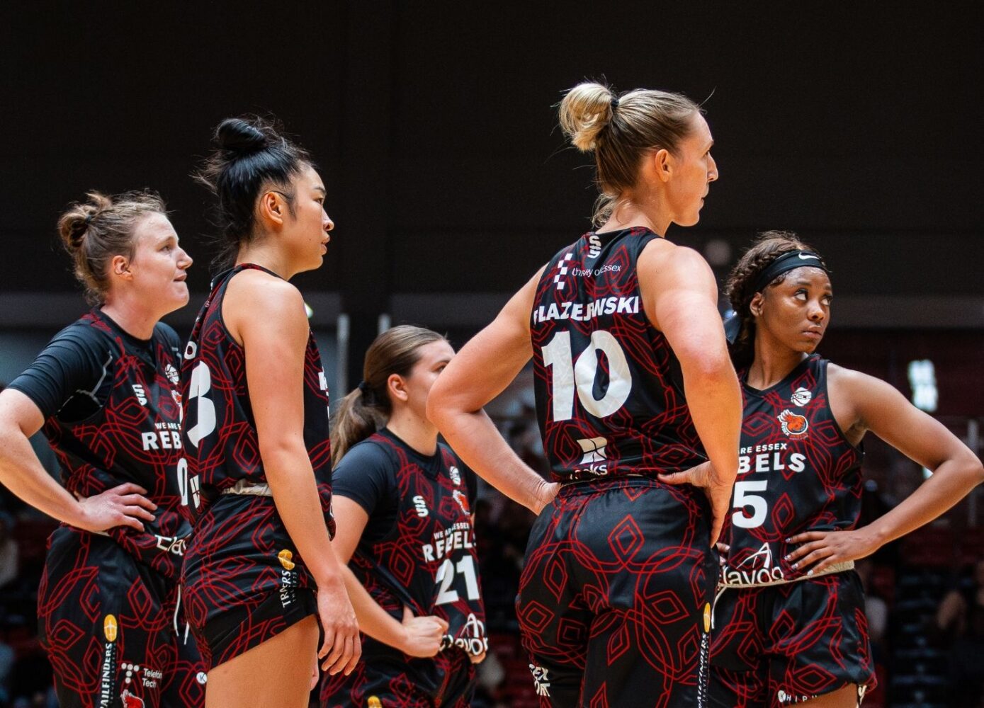 Women's Rebels basketball players on court huddled together with their faces looking across the court (1)
